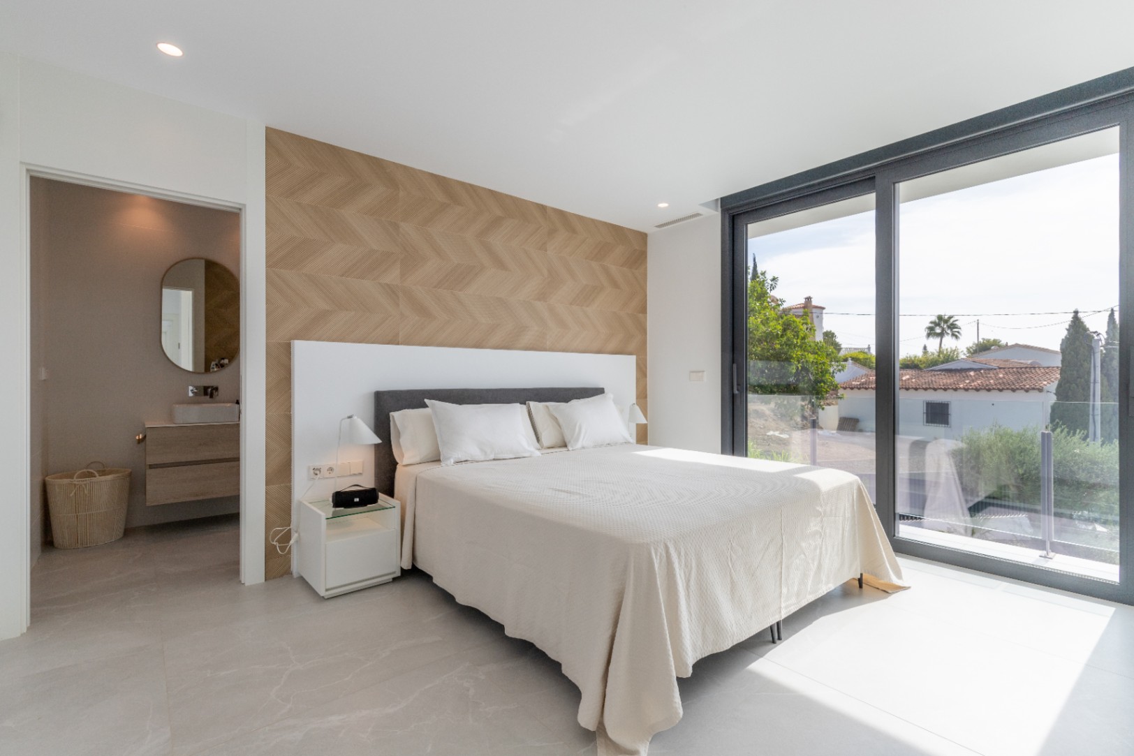 Chambre lumineuse avec mur décoratif à chevrons et accès à la salle de bain attenante. Baie vitrée avec vue.