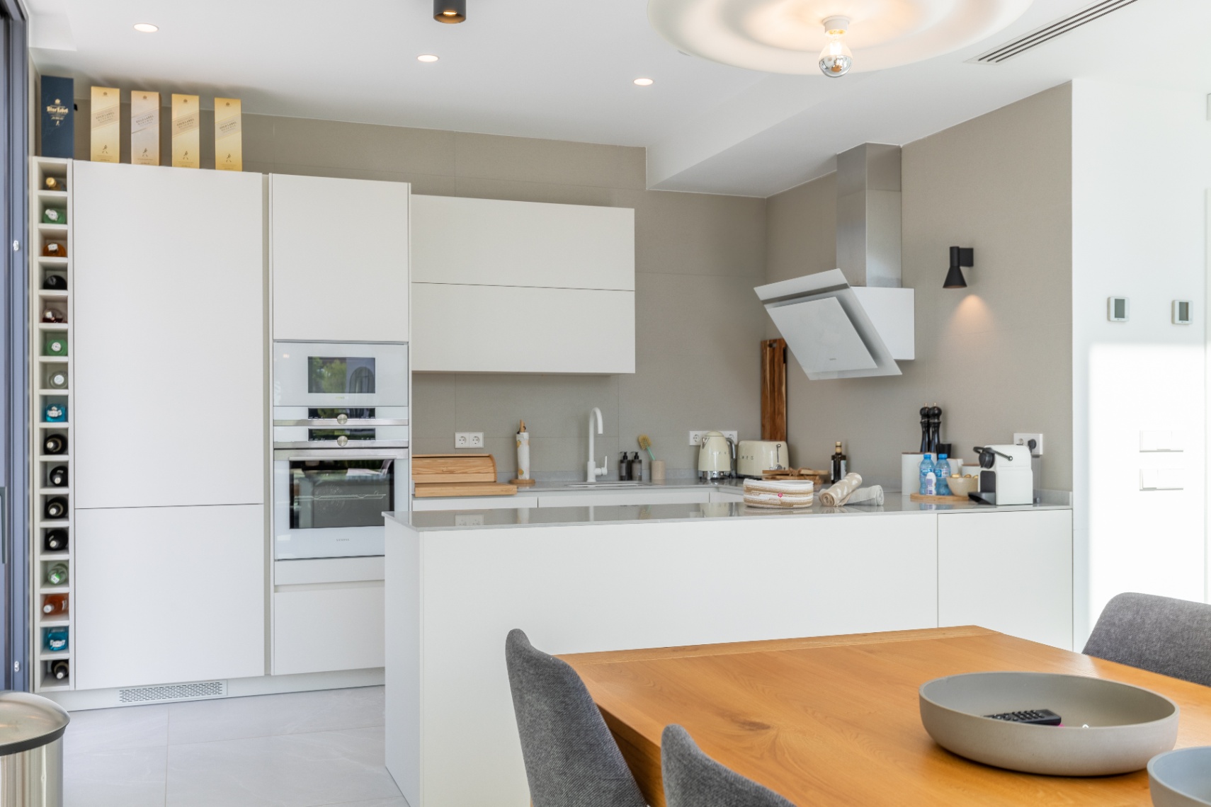 Cuisine moderne avec armoires blanches, électroménagers intégrés et table à manger en bois.