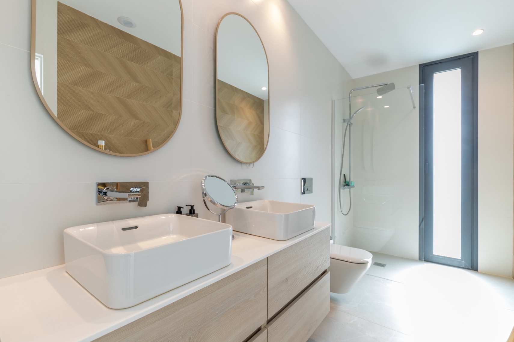 Détail d'une salle de bain moderne avec double vasque, miroirs ovales et douche vitrée.