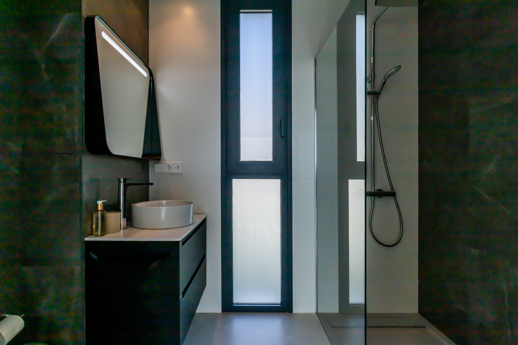 Détail d'une salle de bain moderne avec lavabo en céramique, meuble noir et douche vitrée.