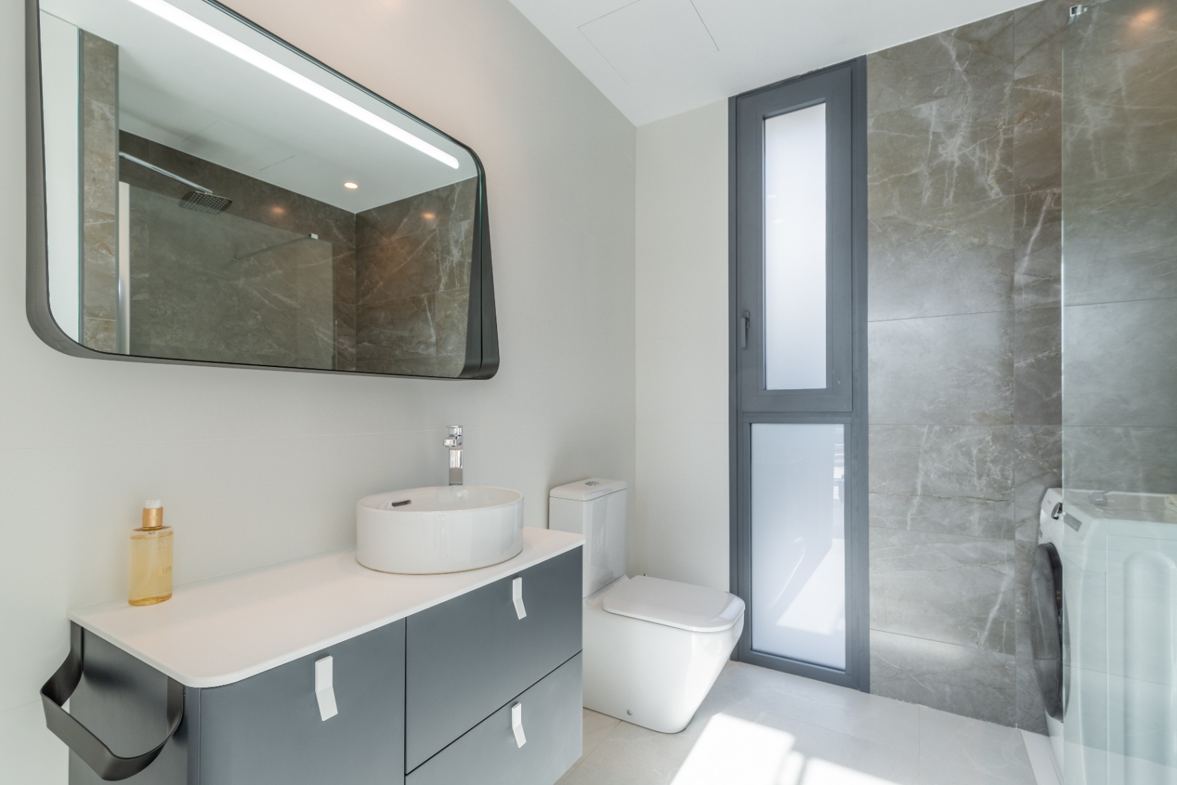 Détail d'une salle de bain moderne avec lavabo en céramique, miroir rétroéclairé et revêtement en marbre gris.