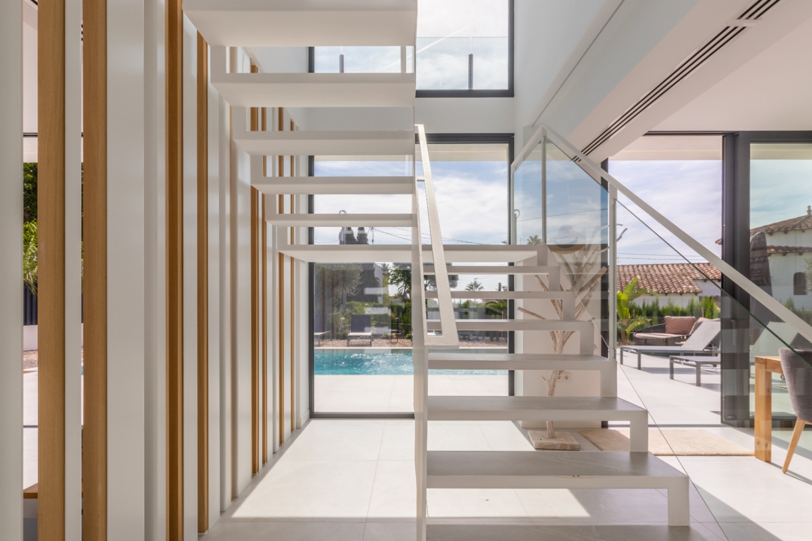 Escalier flottant blanc avec rampe en verre et lattes verticales en bois clair.