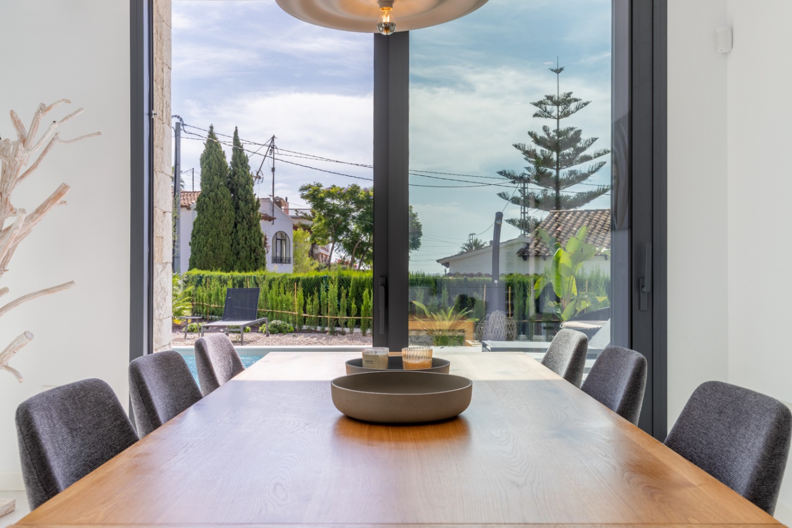 Salle à manger avec table en bois et vue sur la piscine et le jardin clôturé.