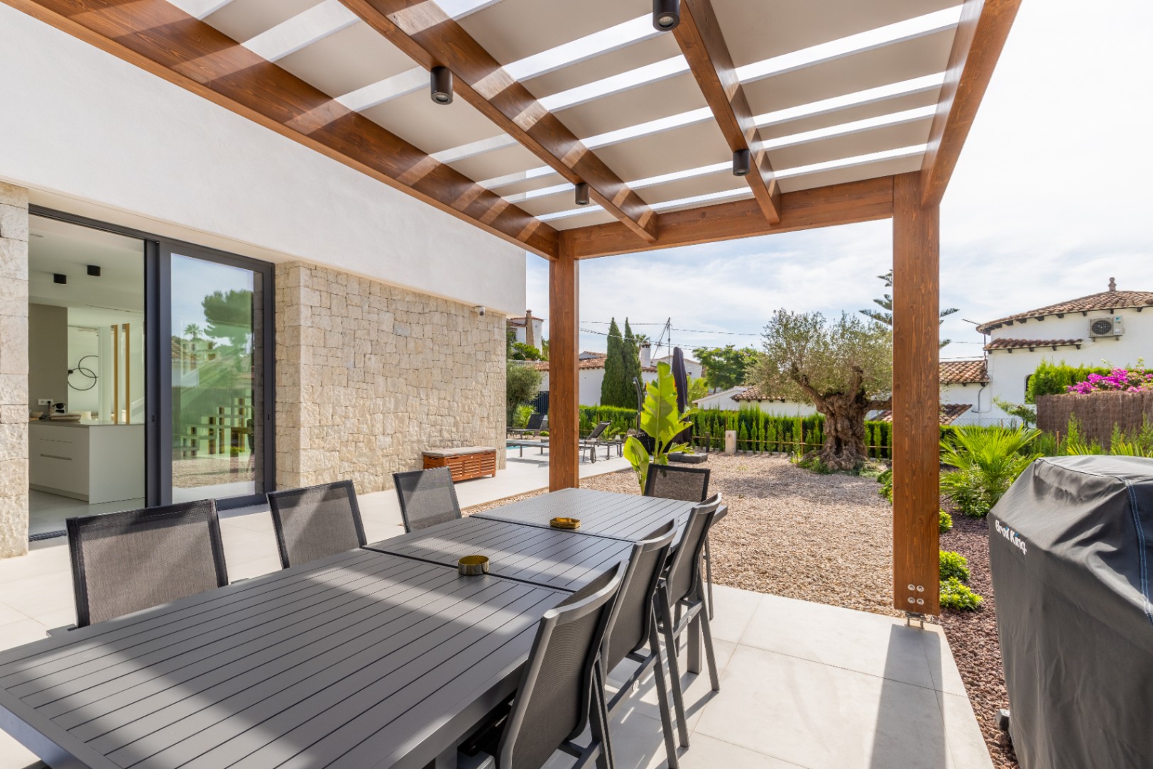 Salle à manger extérieure couverte avec pergola en bois et vue sur le jardin méditerranéen.