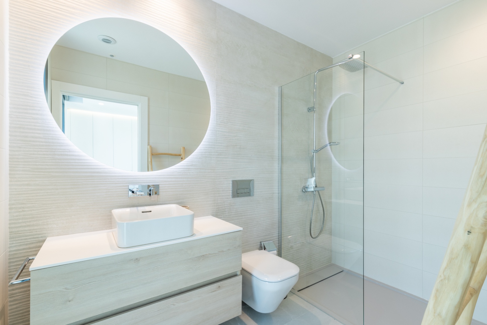 Salle de bain moderne avec lavabo carré, miroir rétroéclairé et douche à parois de verre.