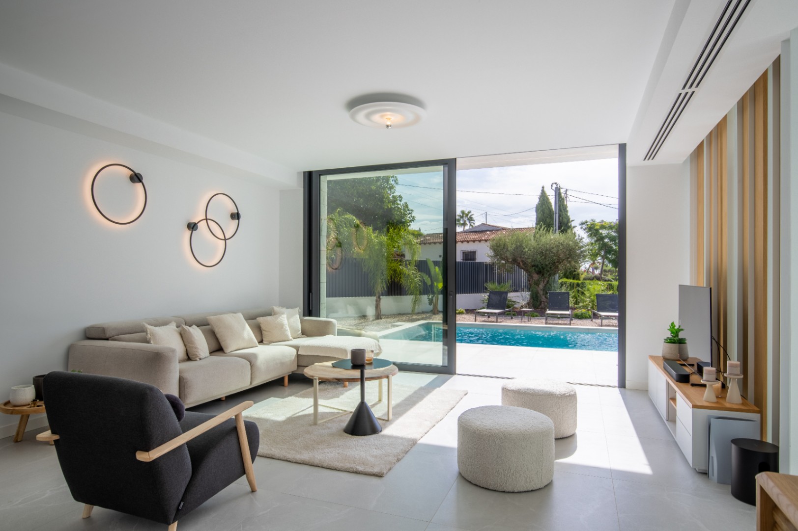 Salon lumineux avec accès direct à la piscine, orné d'appliques murales circulaires et d'un mobilier moderne.