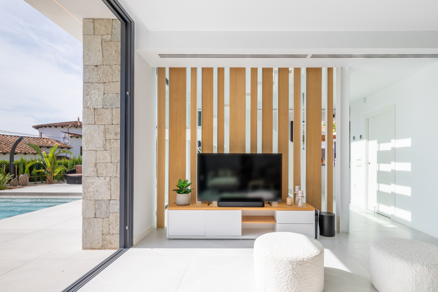 Salon moderne avec meuble TV et claustra en bois clair. Accès à la terrasse avec piscine.