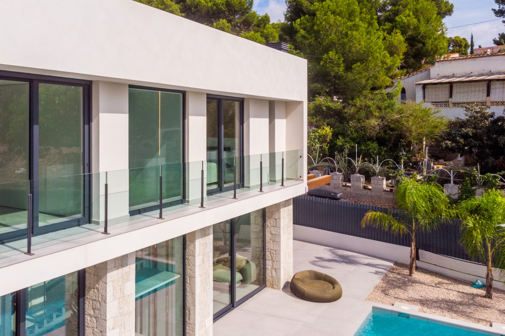 Vue extérieure de la villa avec balcons en verre, parement en pierre et piscine turquoise.