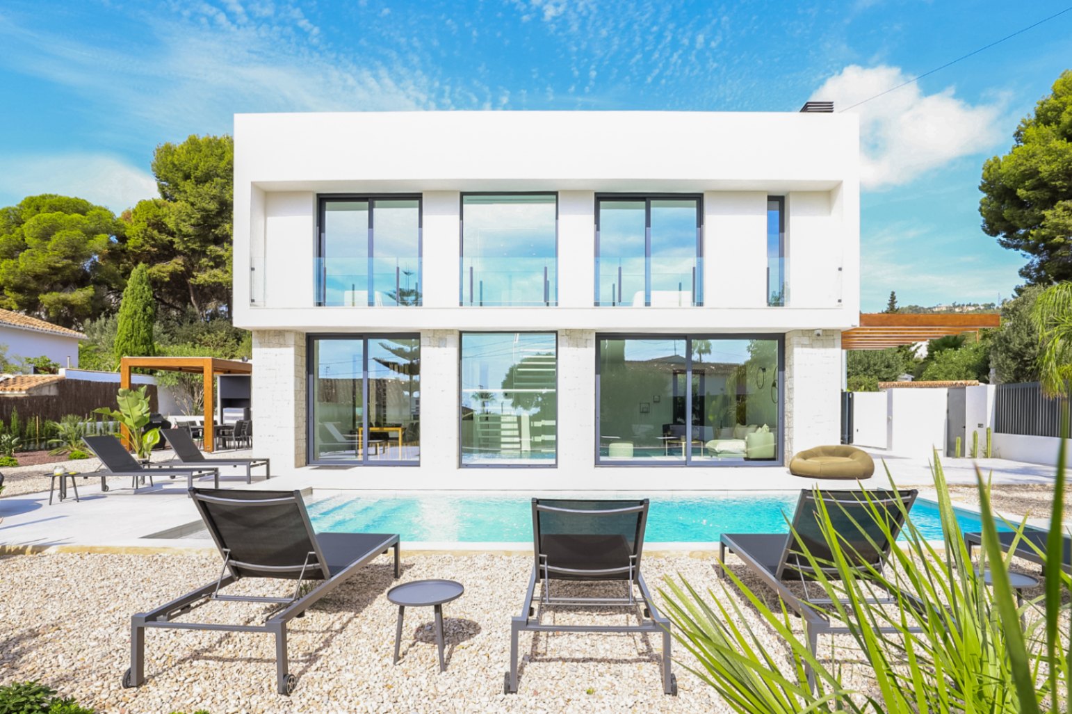Vue extérieure de la villa avec piscine, transats et façade en pierre avec de grandes fenêtres.
