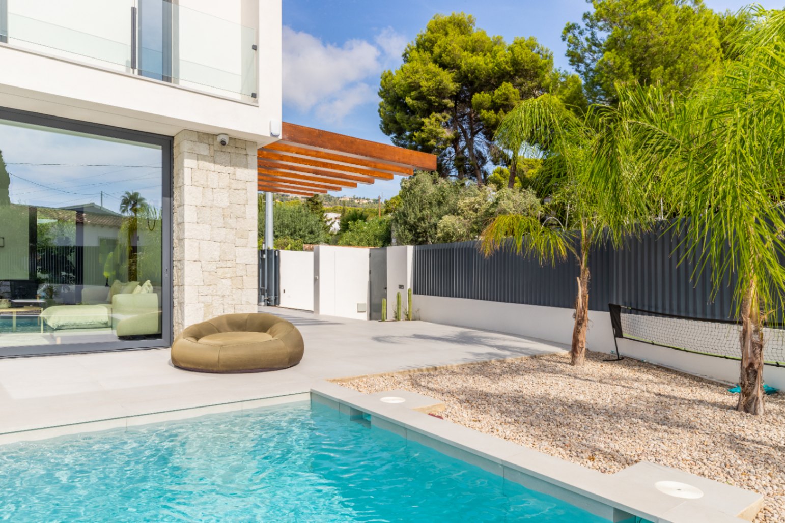 Vue sur la piscine turquoise avec coin salon et façade en pierre claire à Benissa.