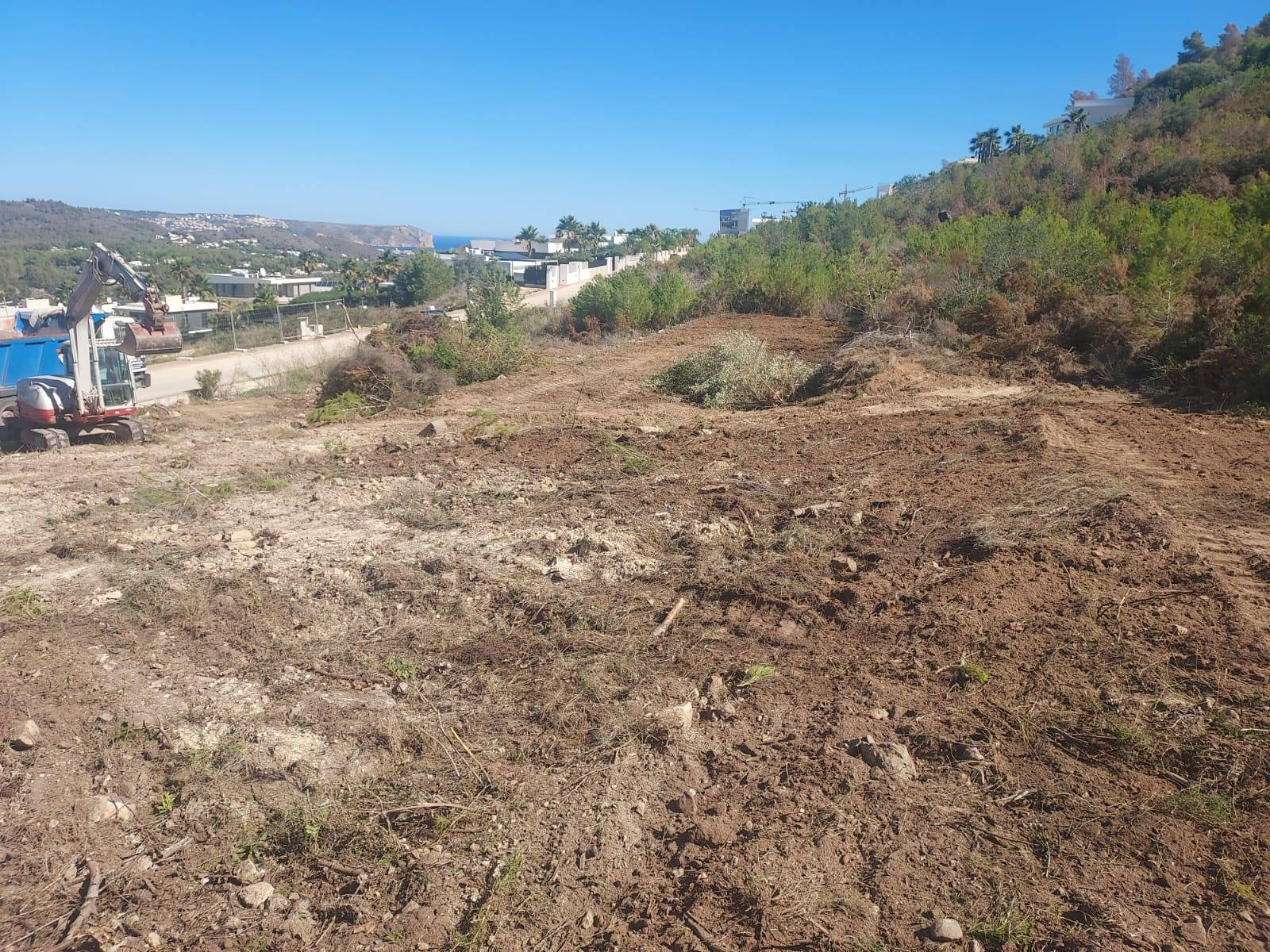 Terrain en préparation à Jávea avec excavatrice et vue sur la mer.