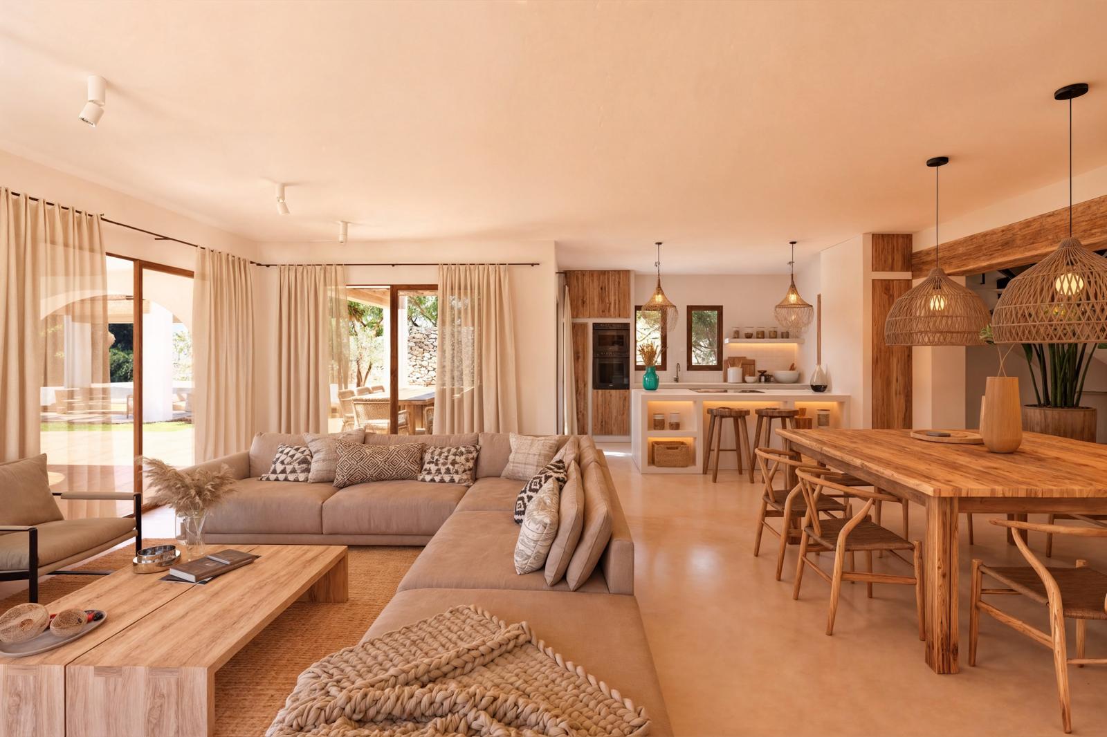 Espace de vie ouvert avec mobilier en bois naturel, canapé d'angle et cuisine intégrée avec îlot blanc. Les suspensions en osier et les grandes baies vitrées apportent une lumière naturelle.