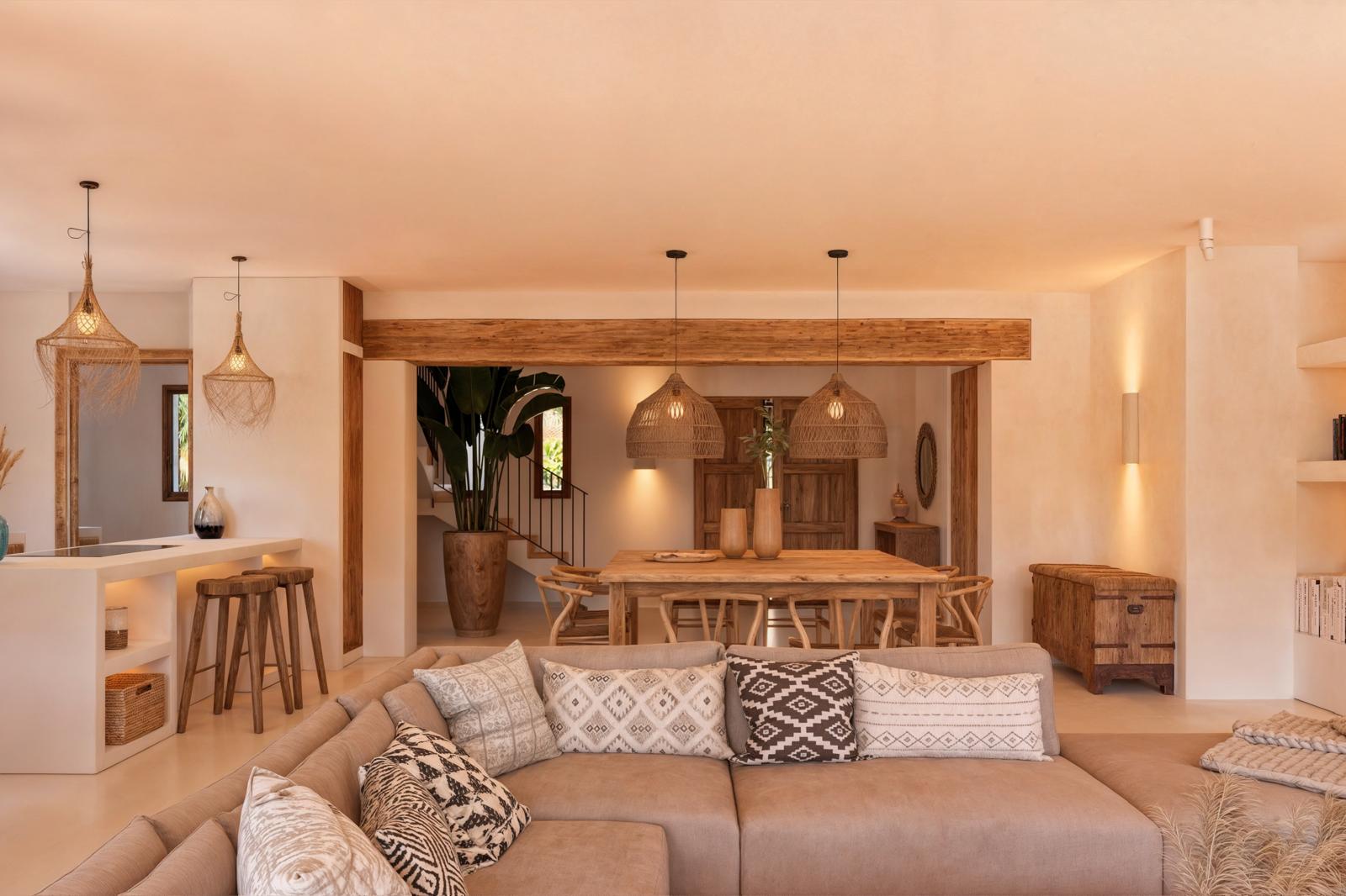 Espace de vie ouvert comprenant un salon et une salle à manger avec poutres en bois, luminaires en fibres naturelles et mobilier aux tons terreux.
