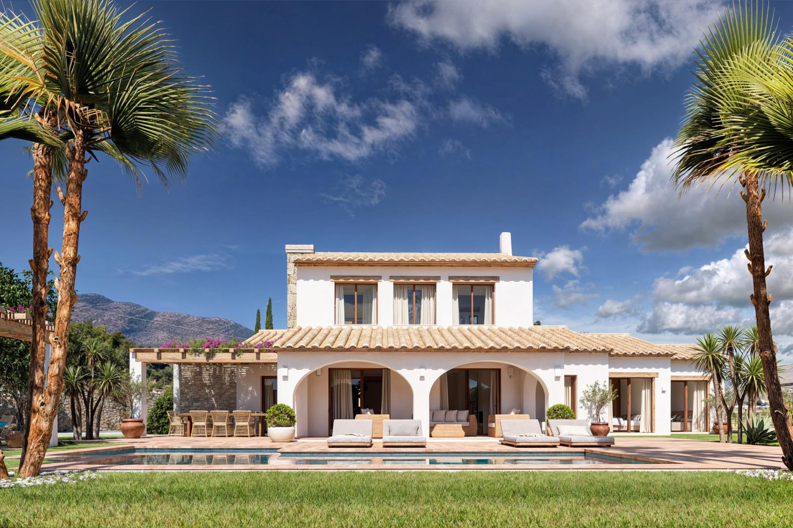 Façade principale de la villa avec porches voûtés, piscine rectangulaire et terrasse en terre cuite, entourée de palmiers et vue sur les montagnes environnantes.