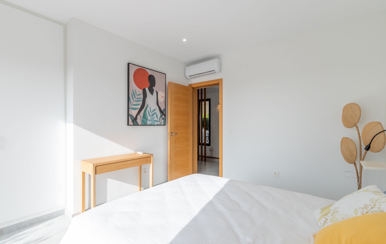 Chambre moderne aux murs blancs avec console en bois naturel et climatisation split. Elle dispose de menuiseries en bois clair et d'une décoration contemporaine.