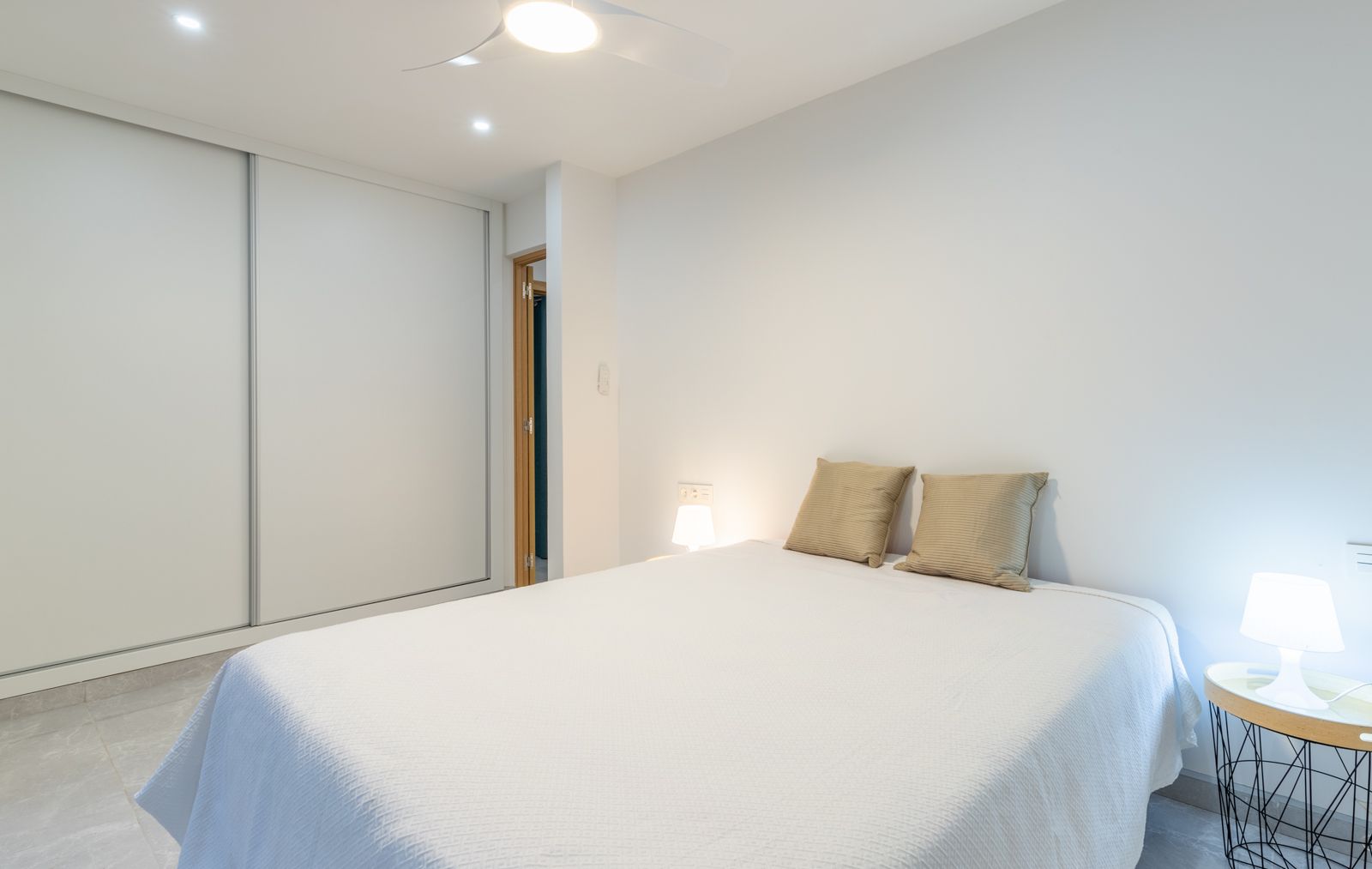 Chambre moderne avec grand placard à portes coulissantes blanches, sol en grès cérame gris et ventilateur de plafond intégré dans un design épuré.