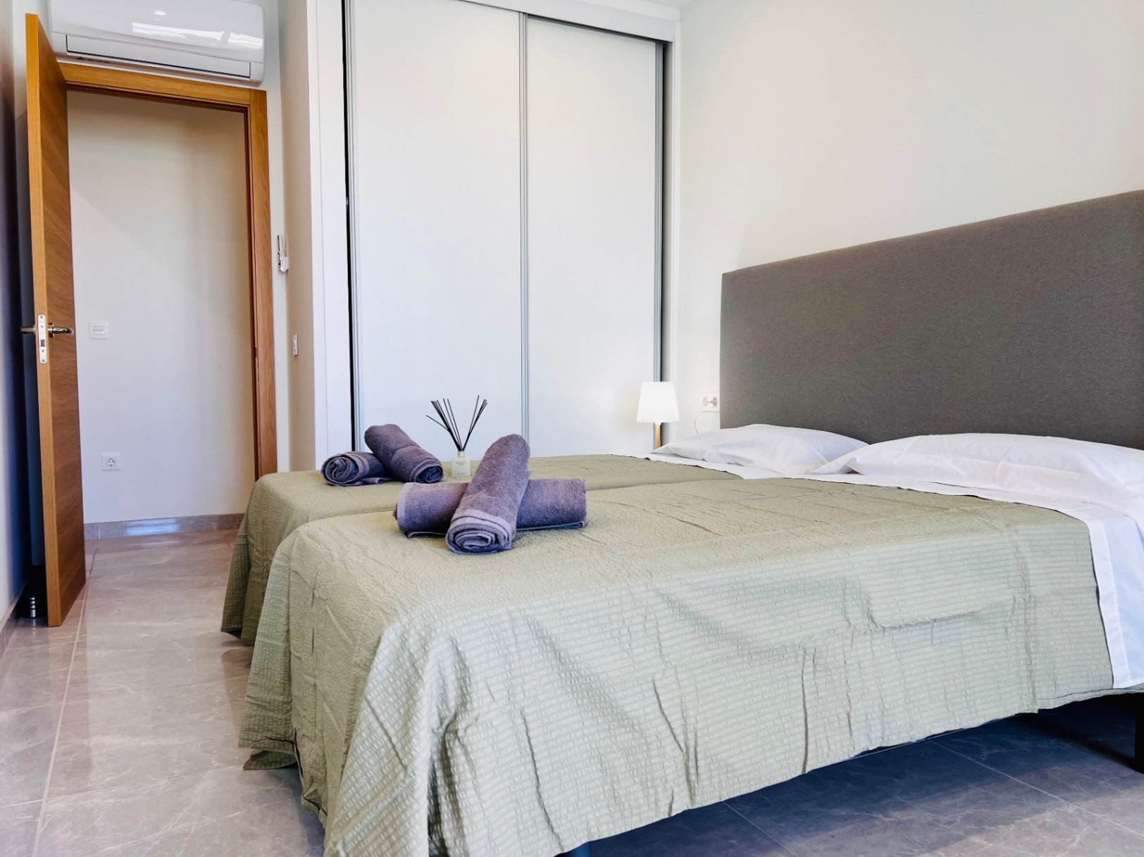 Chambre moderne avec placards intégrés blancs, sol en grès cérame et climatisation individuelle. Finitions soignées incluant une menuiserie intérieure en bois naturel.