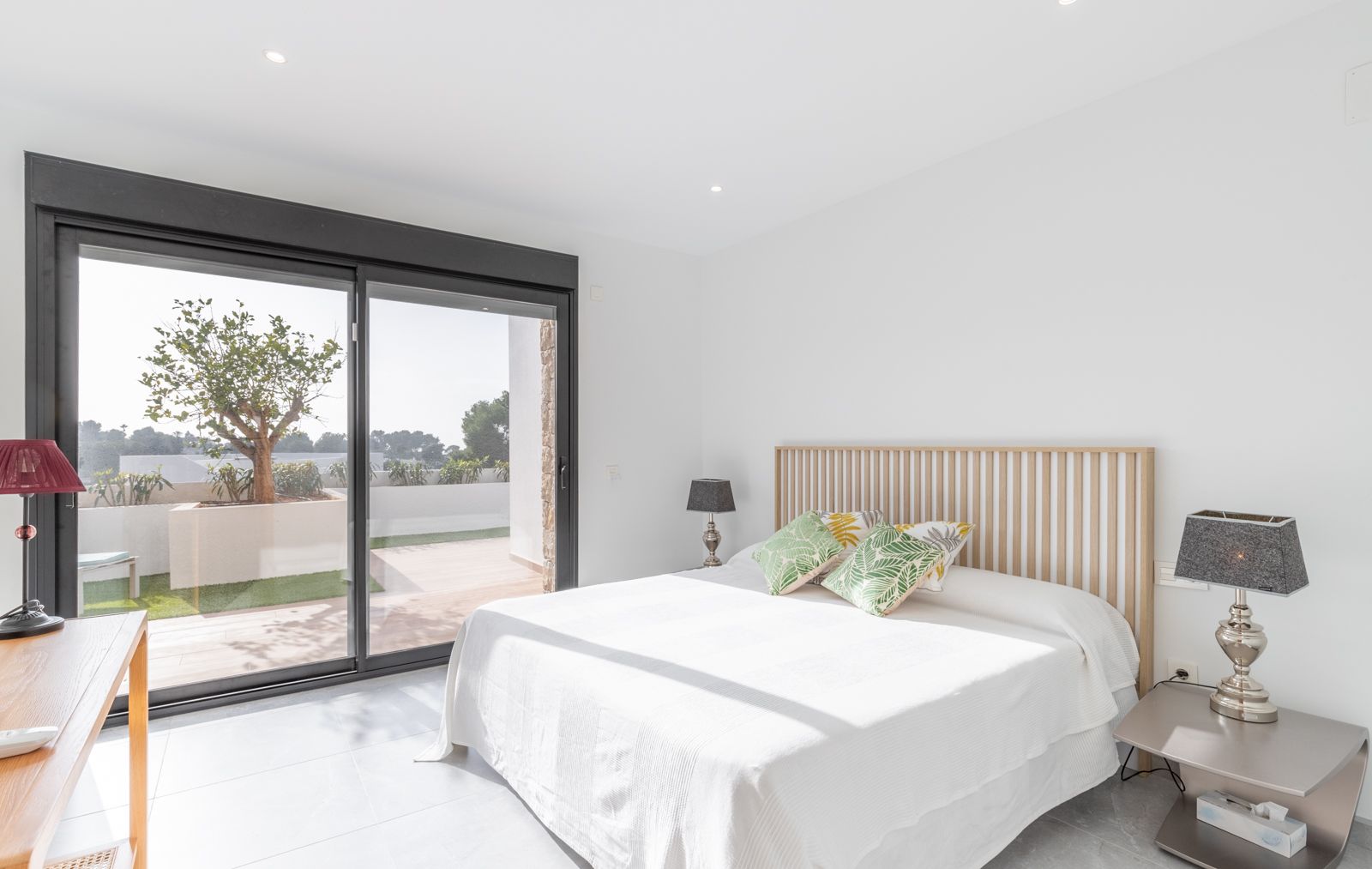 Chambre moderne avec tête de lit en lattes de bois, grandes baies vitrées coulissantes ouvrant sur une terrasse privée et éclairage encastré au plafond.