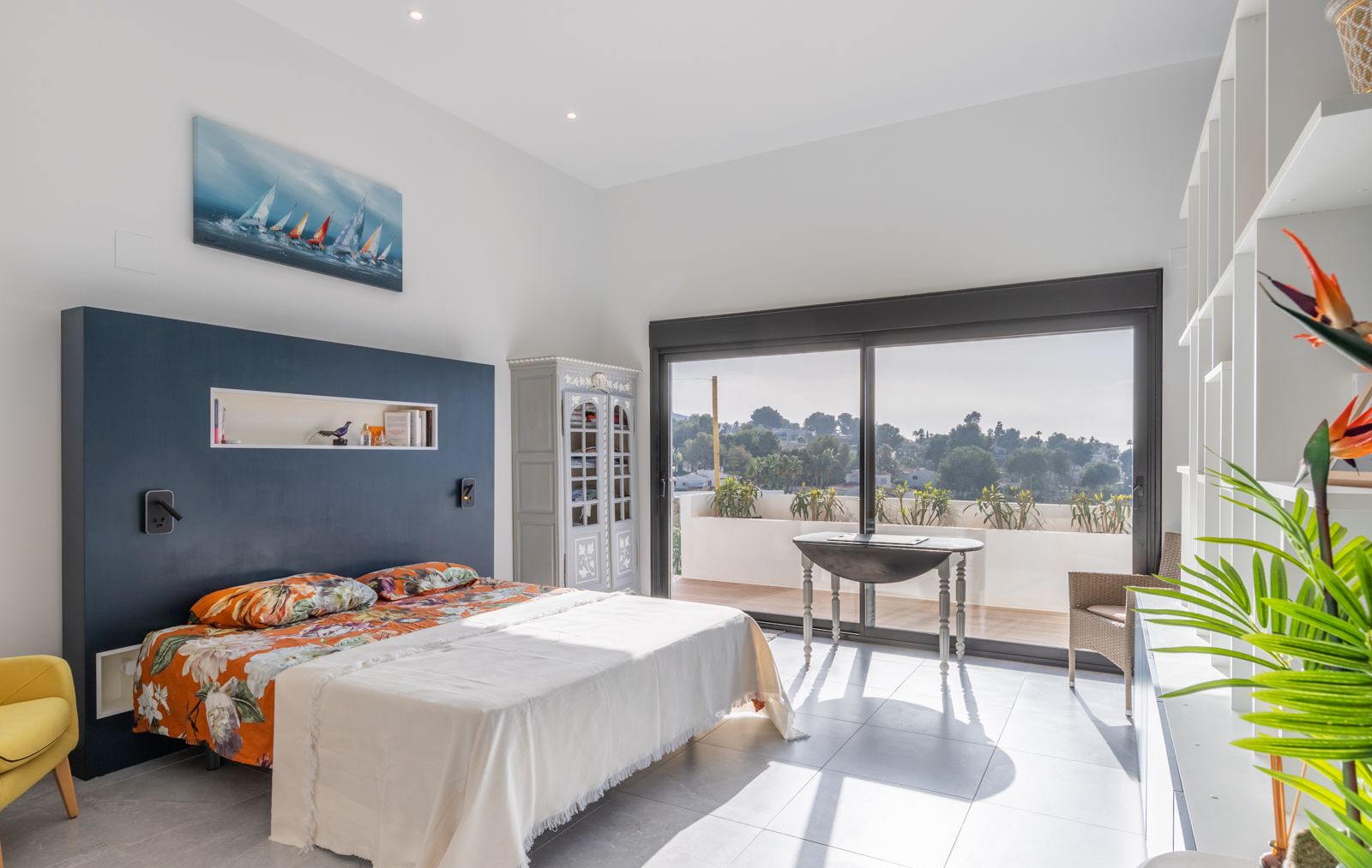 Chambre moderne avec un mur d'accent bleu marine, étagères intégrées et accès direct à une terrasse ensoleillée par de larges baies vitrées.