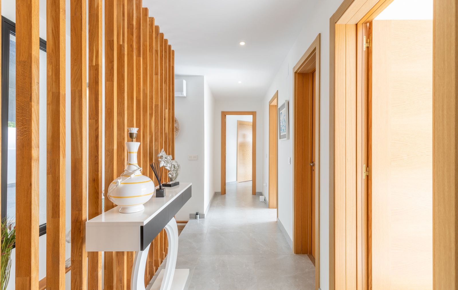 Couloir moderne avec cloison de lattes en bois naturel, sol en grès cérame gris et menuiseries intérieures en bois clair assorties.