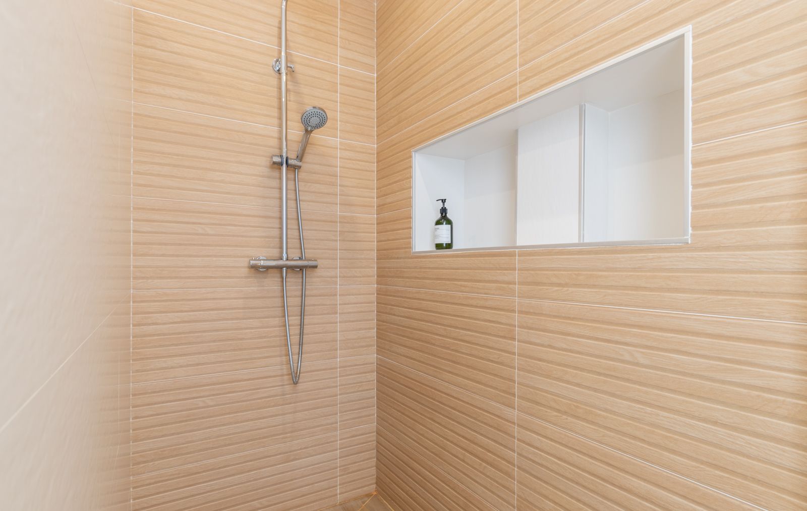 Douche moderne avec revêtement en céramique effet bois, robinetterie chromée et une niche murale encastrée pratique pour les produits de soin.