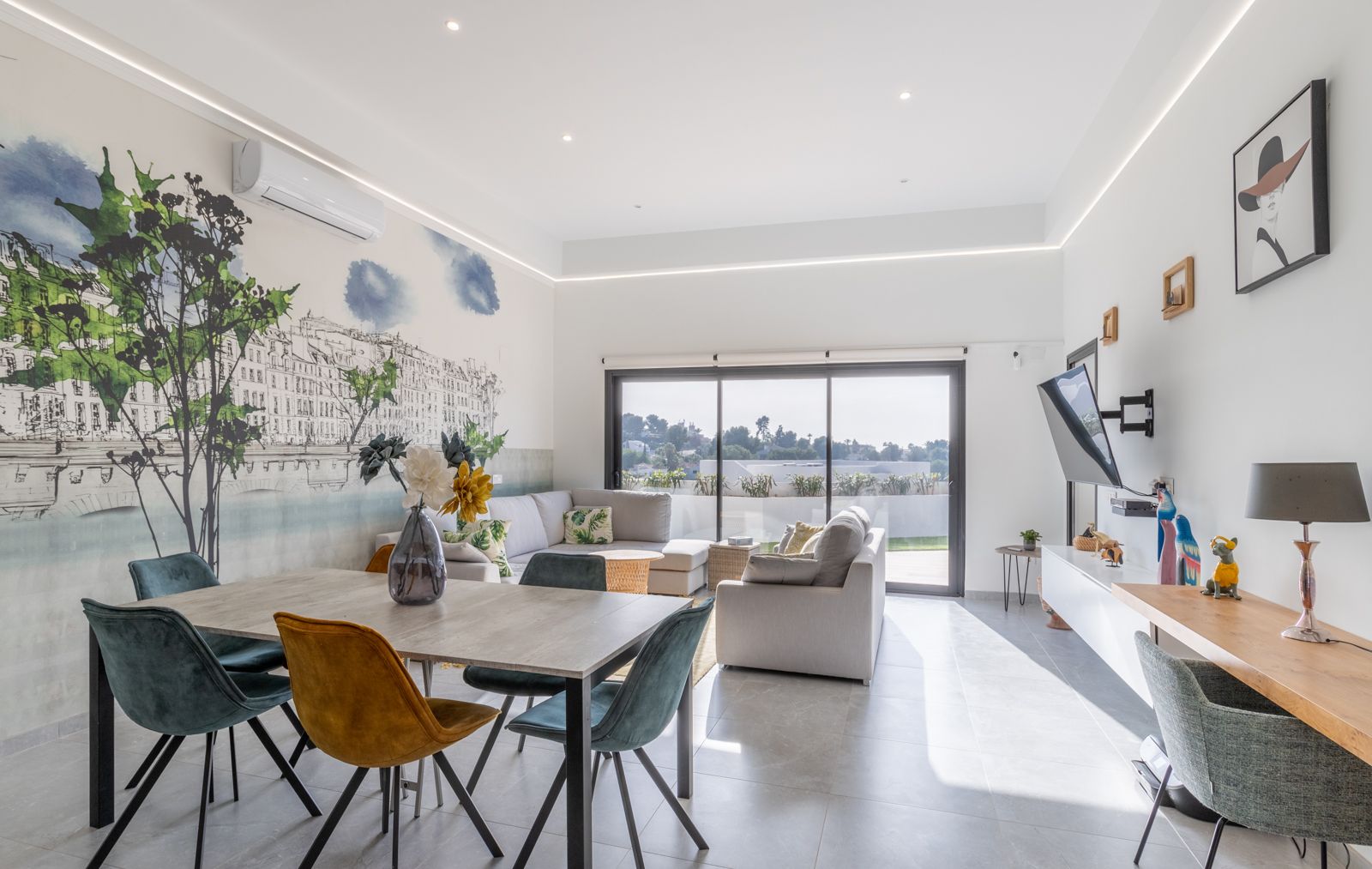 Espace de vie lumineux avec fresque murale, mobilier contemporain et grandes baies vitrées offrant un accès direct à la terrasse extérieure.