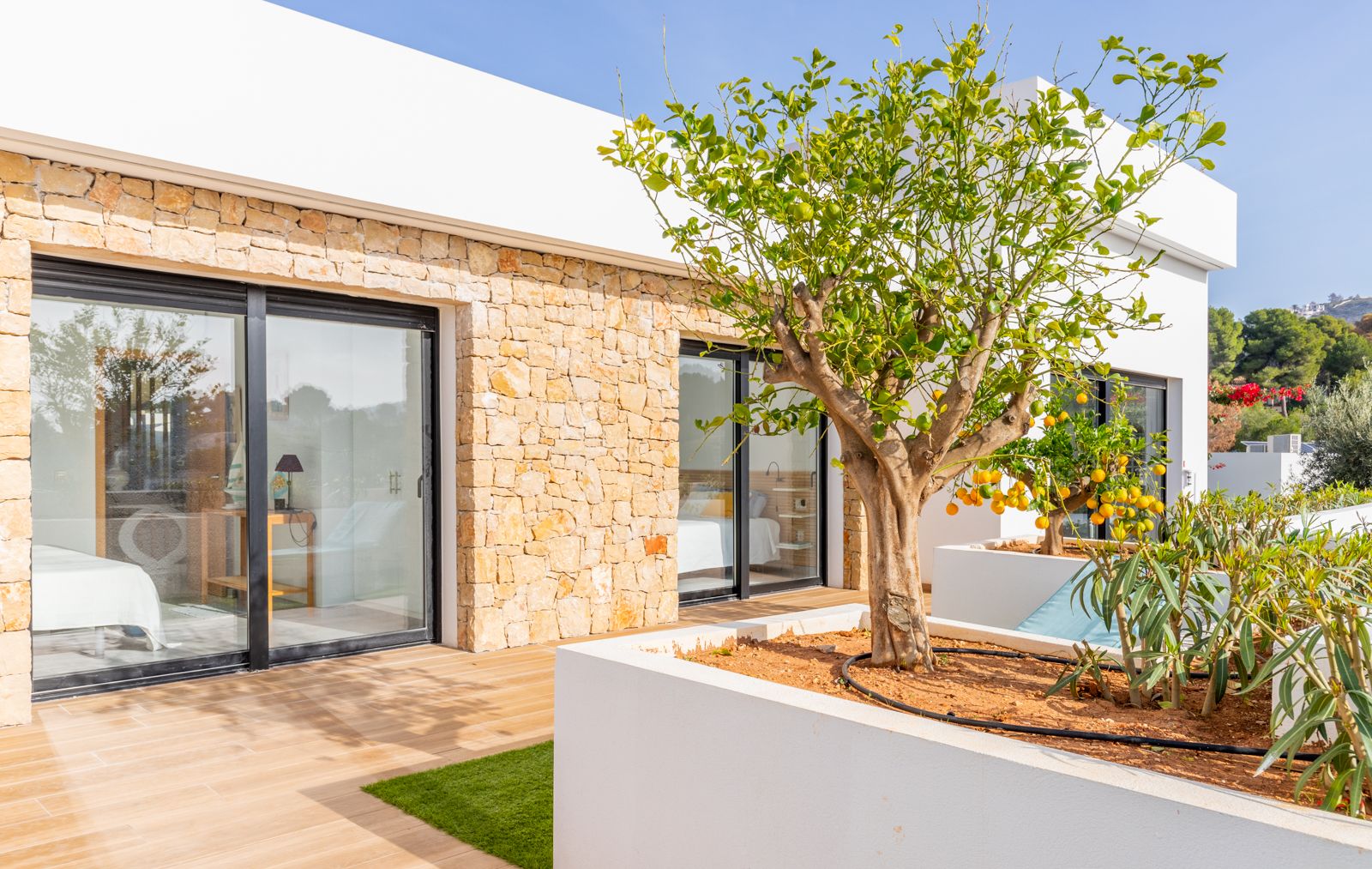 Façade moderne alliant pierre naturelle et murs blancs, avec de larges baies vitrées ouvrant sur une terrasse agrémentée d'un citronnier en jardinière.