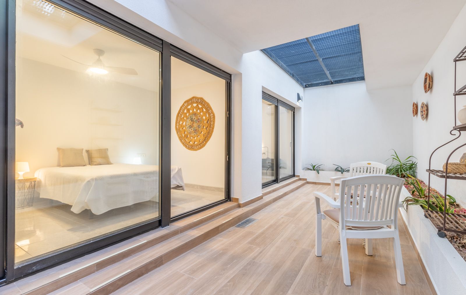 Patio intérieur avec carrelage effet bois, coin salon et grandes baies vitrées donnant sur une chambre lumineuse au design épuré.