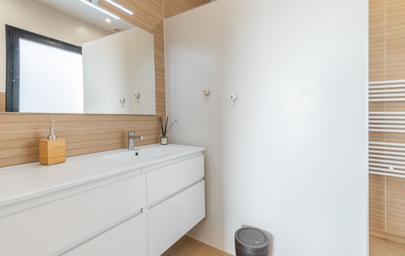 Salle de bain moderne avec meuble vasque suspendu blanc, carrelage mural aspect bois et miroir avec éclairage LED intégré. Comprend un radiateur sèche-serviettes blanc.