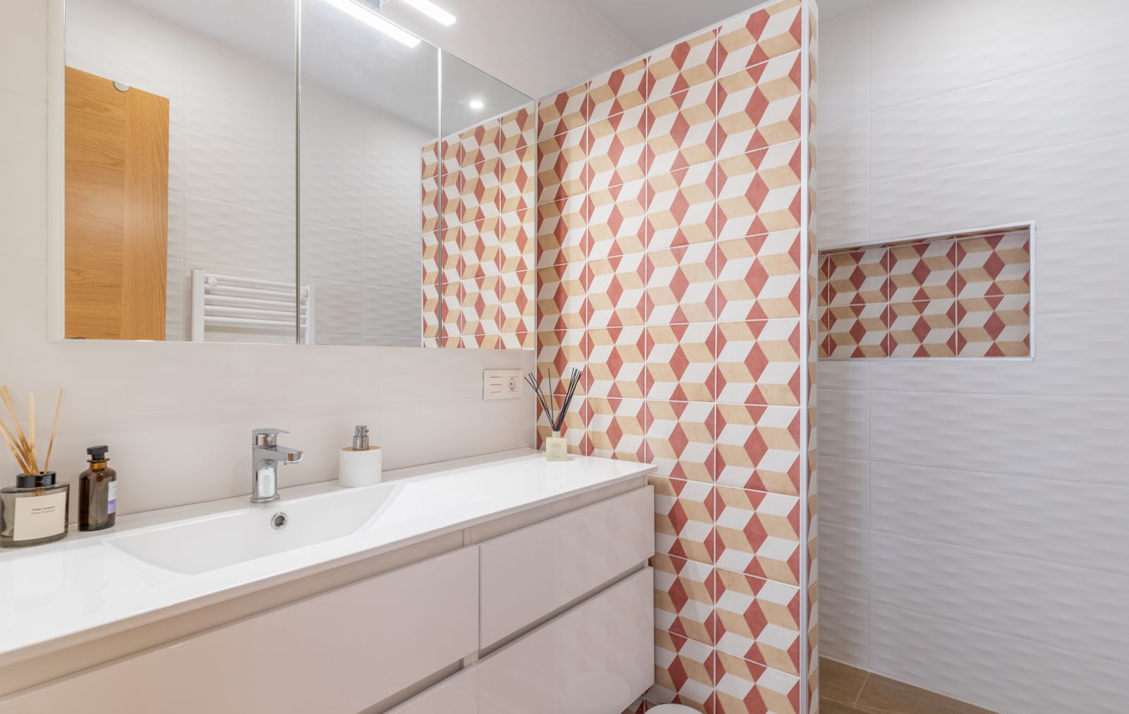 Salle de bains moderne avec meuble vasque blanc, armoire de toilette miroir et mur d'accent aux motifs géométriques avec niche intégrée.