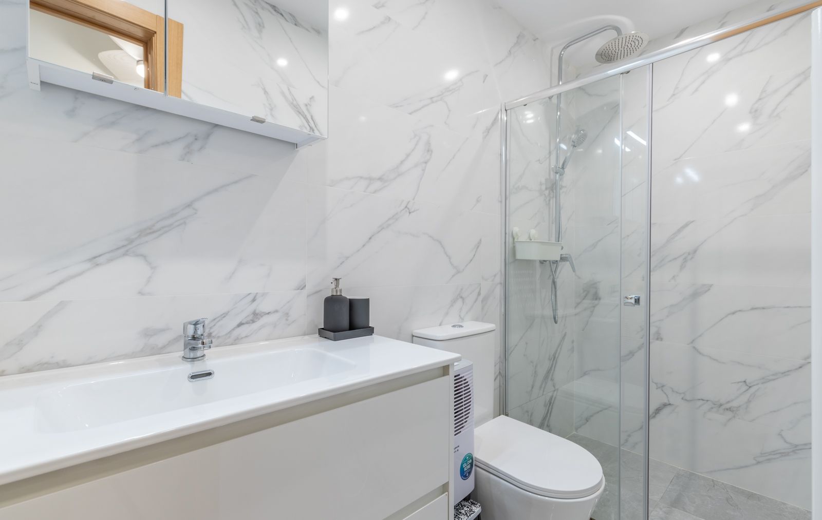 Salle d'eau contemporaine avec murs en grès cérame effet marbre, meuble vasque blanc et douche à l'italienne avec paroi vitrée et robinetterie chromée.