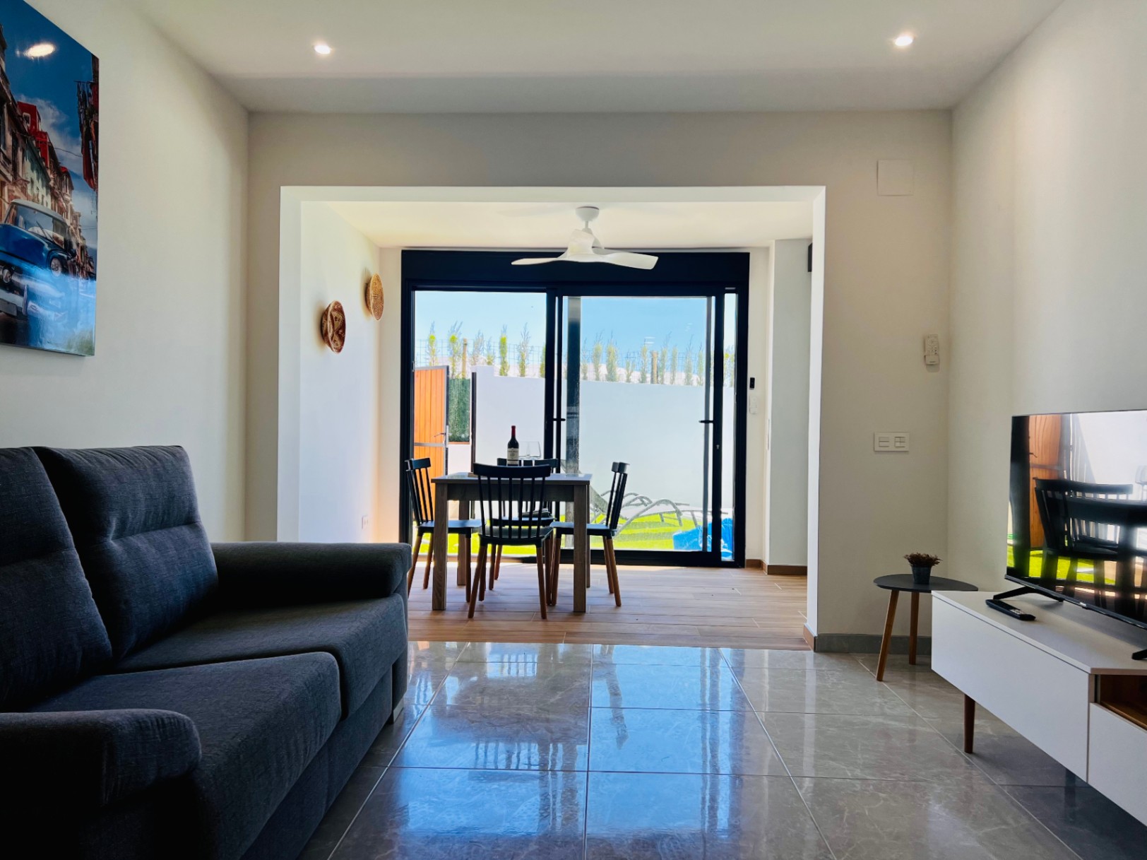 Séjour contemporain avec sol en grès poli, canapé gris et coin repas intégré doté d'un ventilateur de plafond et d'un accès direct à la terrasse.