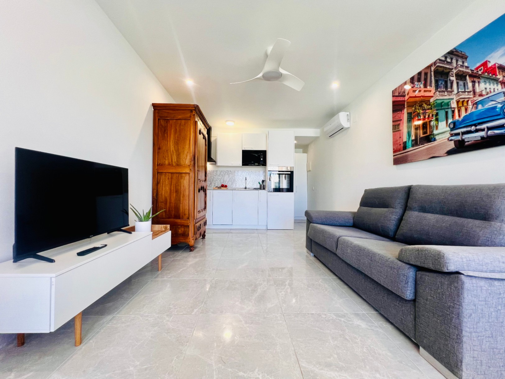 Séjour d'un appartement d'invités avec sol en grès cérame effet marbre, canapé gris, kitchenette blanche moderne et armoire en bois de style classique.