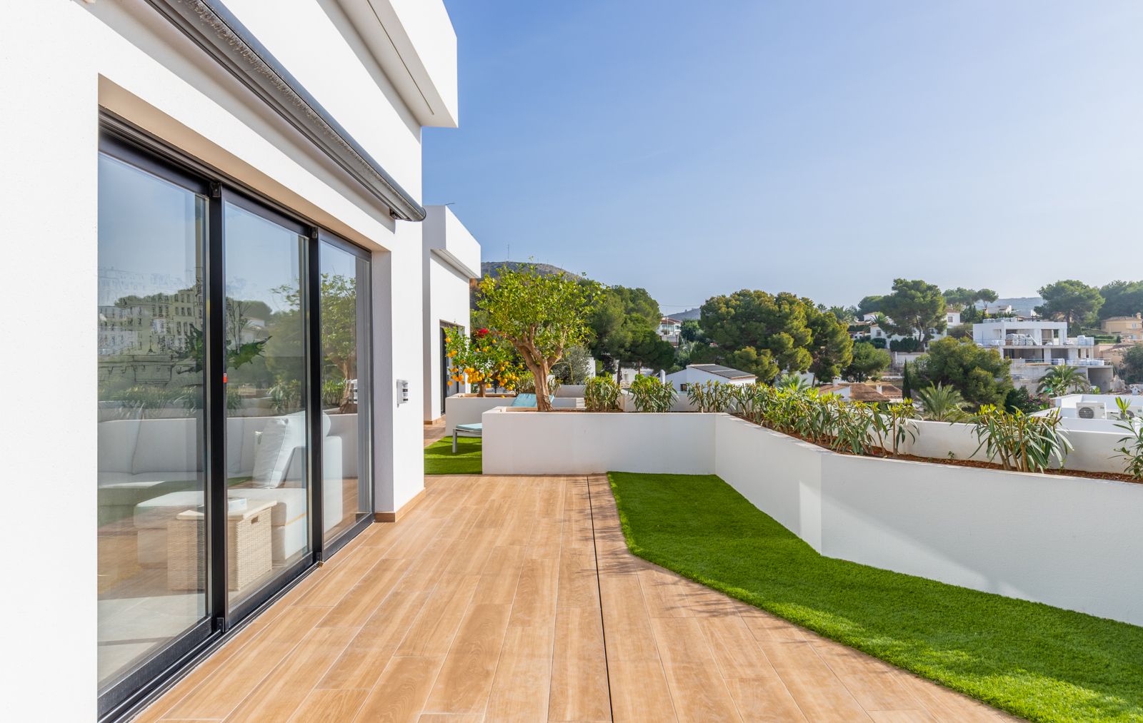 Terrasse supérieure avec revêtement en grès cérame aspect bois, zones de gazon synthétique et jardinières intégrées offrant une vue sur le quartier.