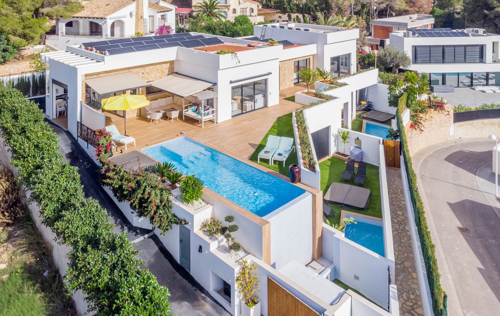 Vue aérienne de la villa moderne avec piscine à débordement, terrasses en bois, panneaux solaires en toiture et espaces extérieurs privés pour les invités.