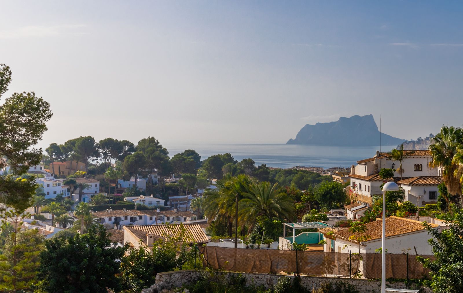 Vue panoramique sur la mer Méditerranée et le Peñón de Ifach, dominant un quartier résidentiel avec villas blanches et végétation méditerranéenne.
