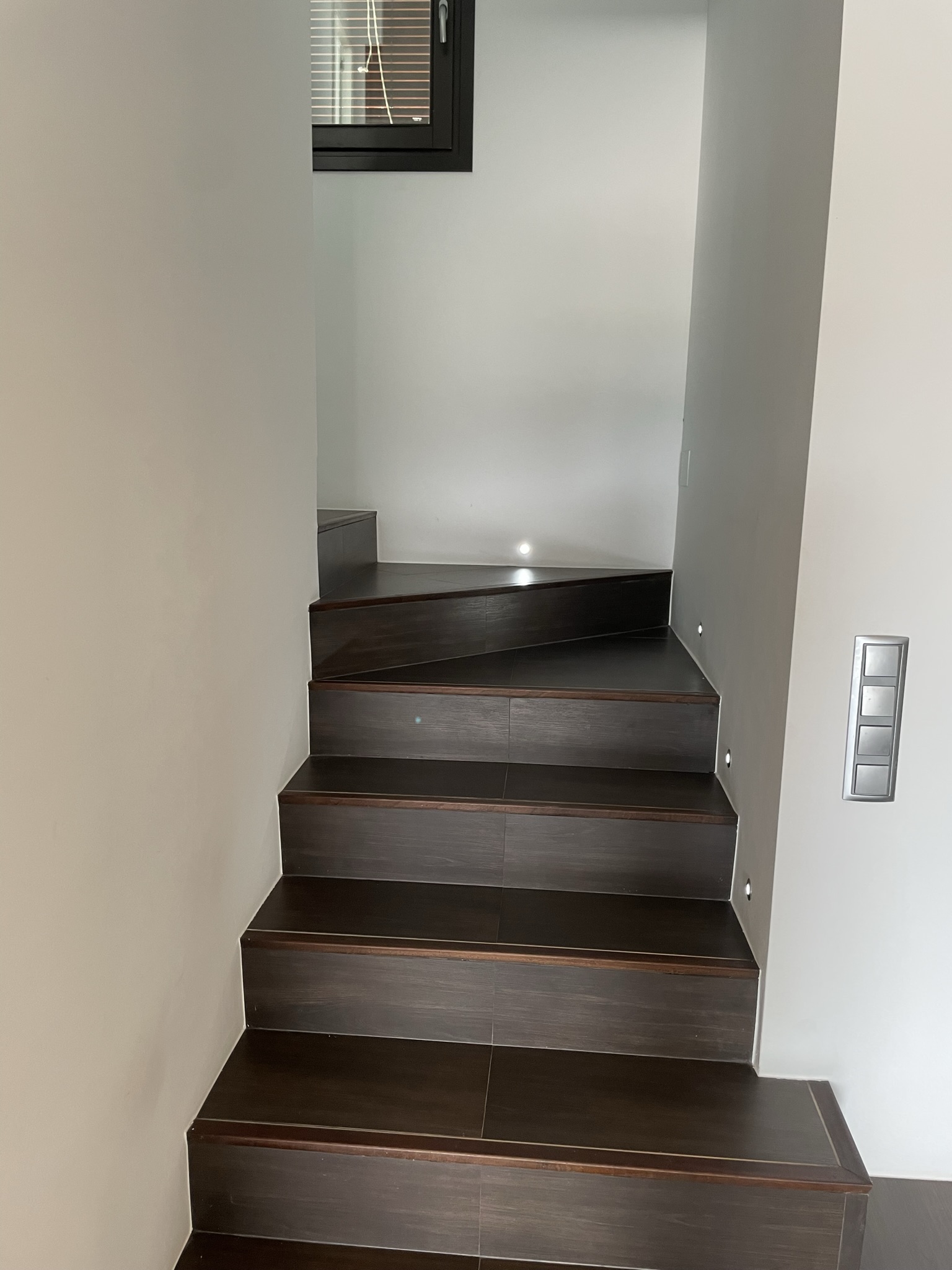 Escalier intérieur aux marches sombres avec éclairage LED encastré dans le mur, offrant un design moderne et épuré vers l'étage.