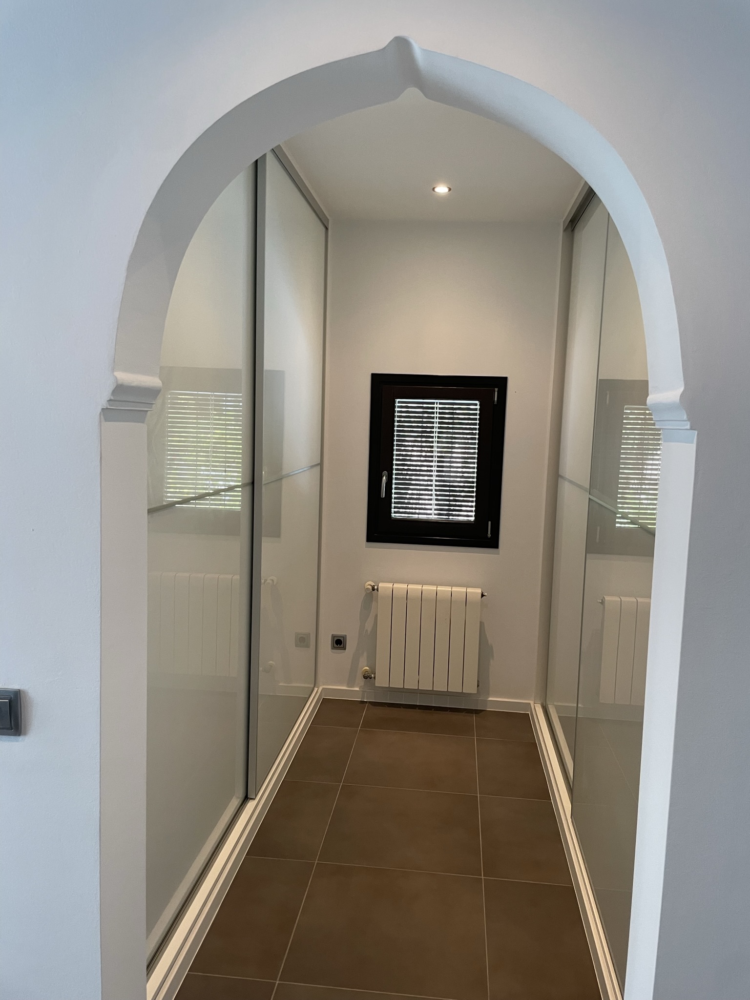 Espace dressing avec placards intégrés à portes coulissantes, encadré par une arche méditerranéenne et doté d'un radiateur pour un confort thermique optimal.