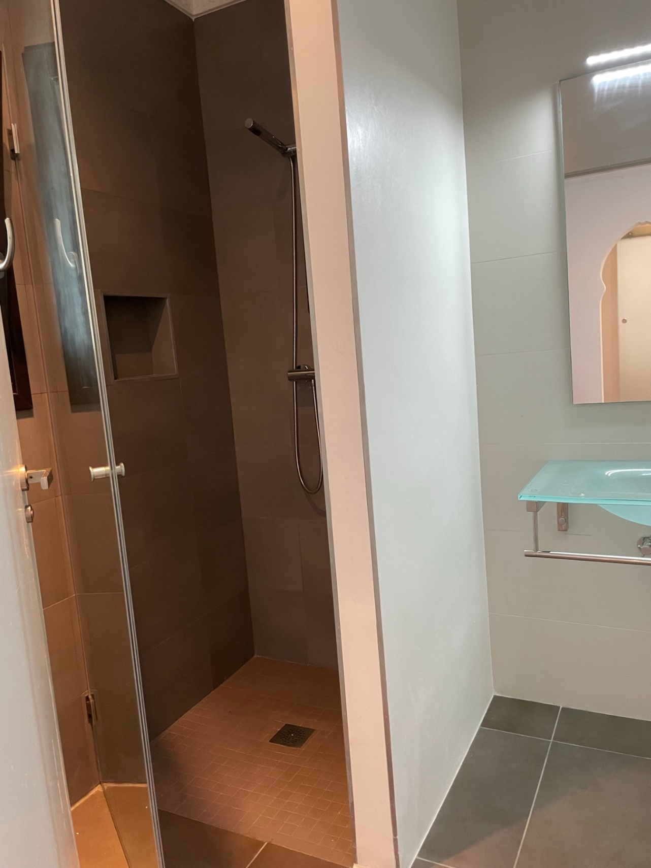 Salle de bain moderne avec douche à l'italienne aux tons terreux, niche murale intégrée et lavabo en verre suspendu.