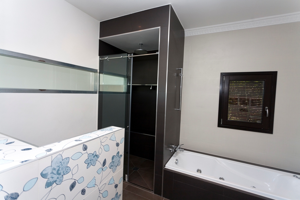 Salle de bain moderne équipée d'une baignoire et d'une douche séparée. Elle se distingue par son carrelage chocolat et sa paroi décorative aux motifs floraux bleus.