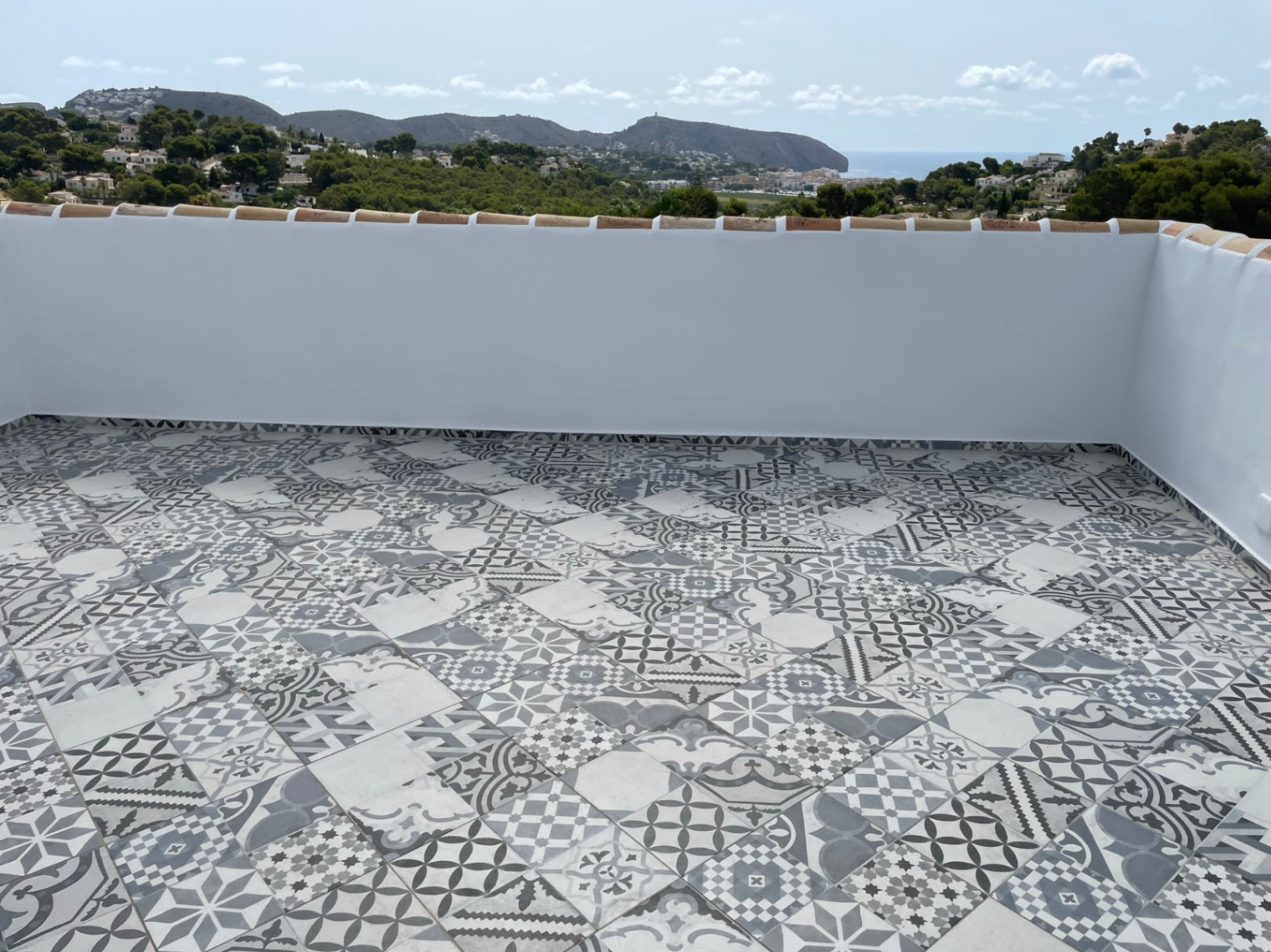 Terrasse solarium avec carrelage à motifs géométriques offrant une vue panoramique sur la mer Méditerranée et la côte de Moraira.