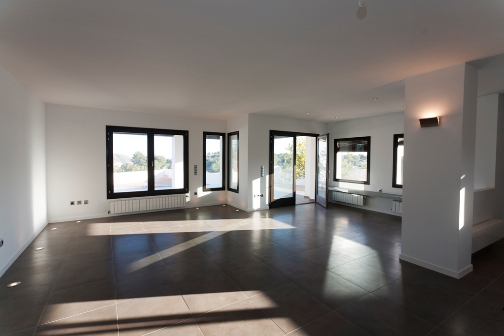 Vaste salon-salle à manger avec carrelage sombre, éclairage au sol intégré et grandes fenêtres offrant une lumière naturelle généreuse et un accès extérieur.