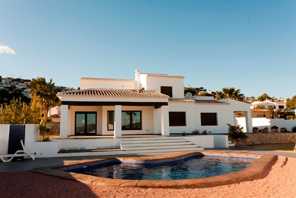 Vue extérieure de la villa avec piscine de forme libre, terrasse couverte à poutres apparentes et façade blanche de style méditerranéen.