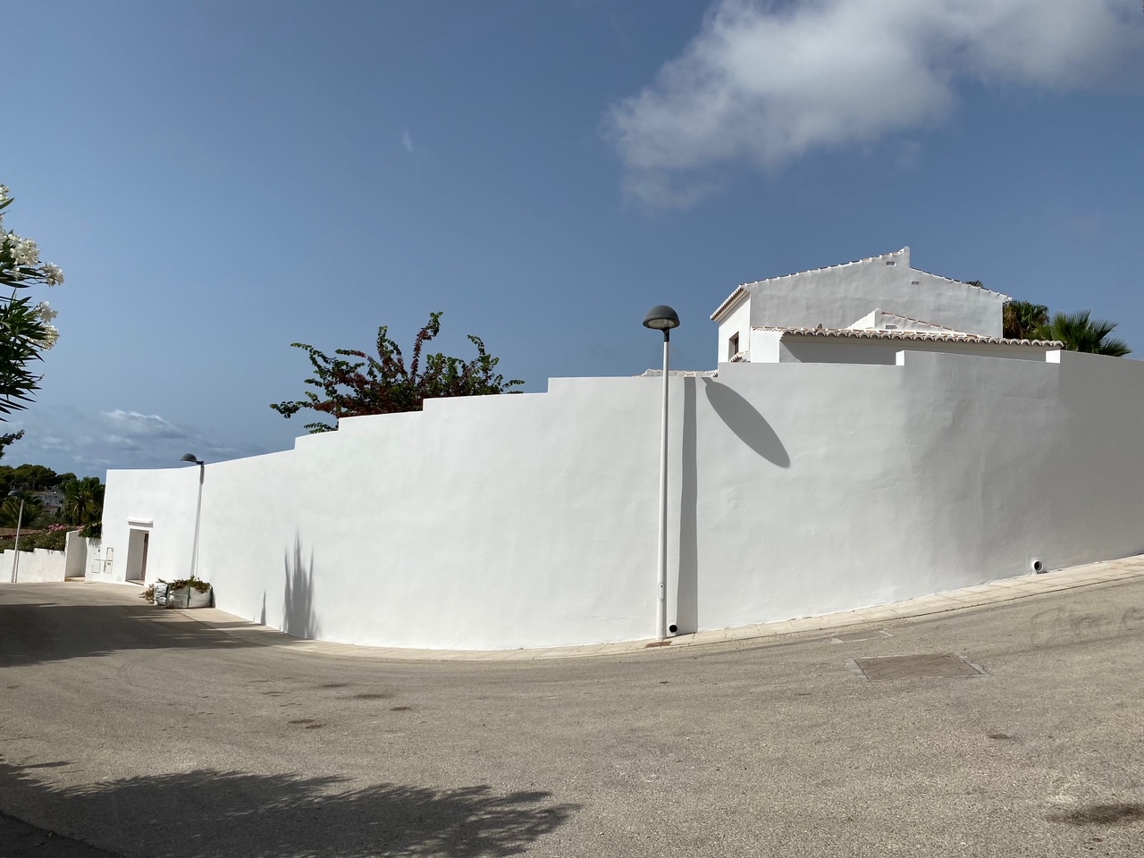 Vue extérieure mettant en avant le haut mur d'enceinte blanc au design en escalier, offrant une intimité totale à la villa depuis la rue résidentielle.