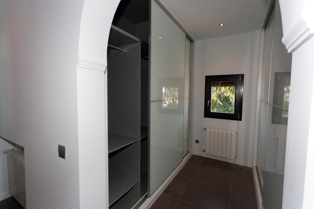 Zone de dressing avec placards intégrés à portes coulissantes en verre dépoli, étagères intérieures, sol en grès foncé, radiateur et éclairage encastré.