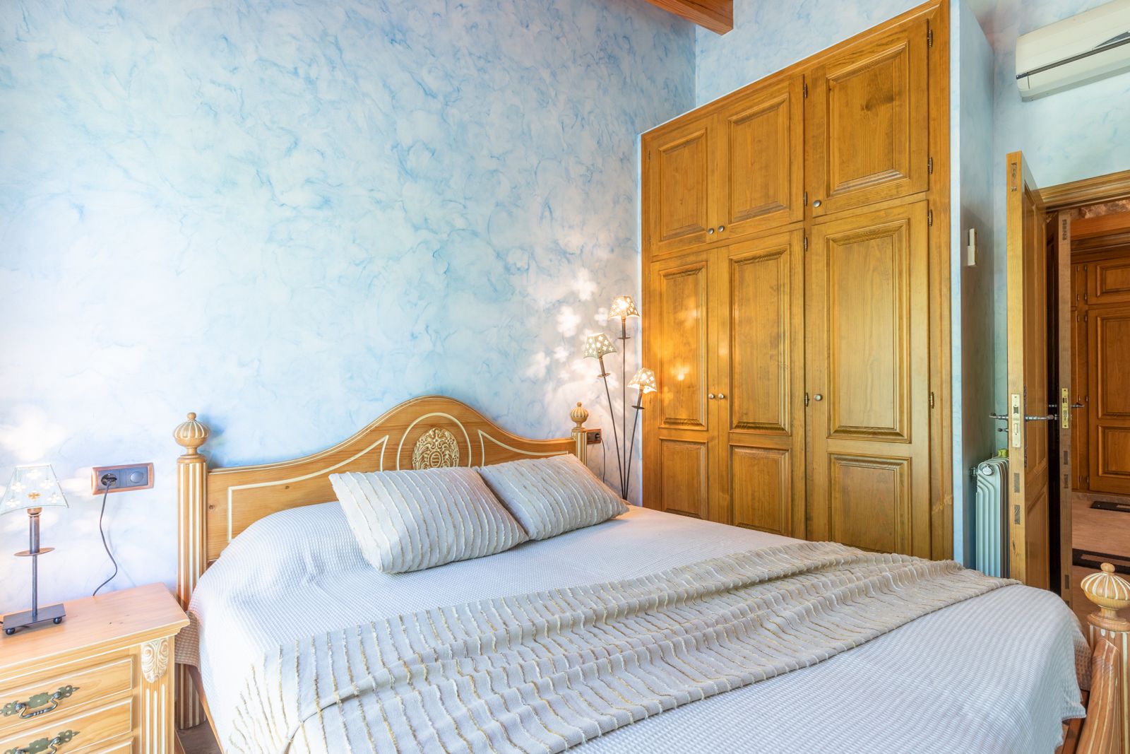 Chambre avec mur bleu texturé, cadre de lit en bois clair et armoire encastrée en bois.