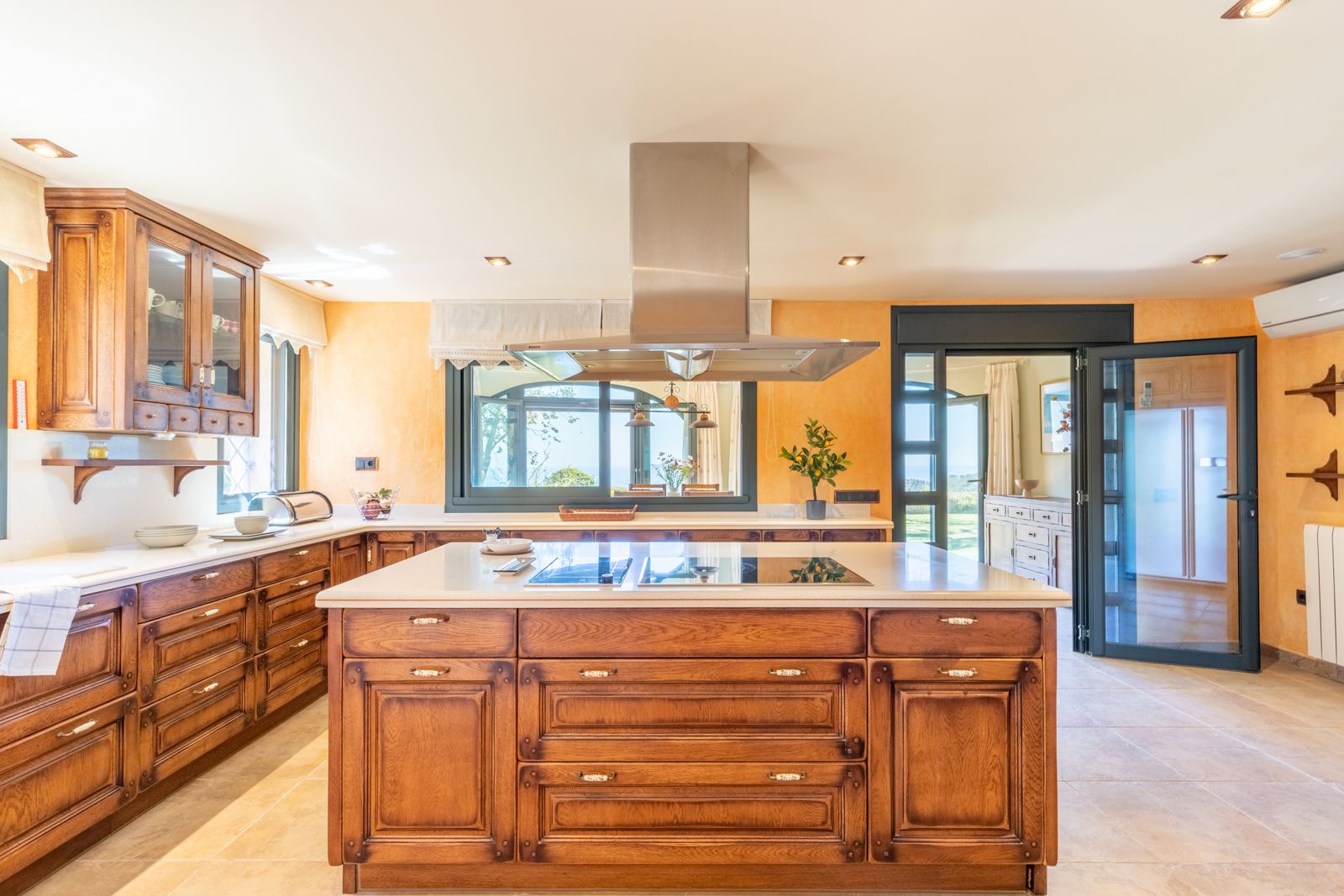Cuisine rustique avec îlot central en bois, comptoir clair, hotte en acier et vue sur l'extérieur.