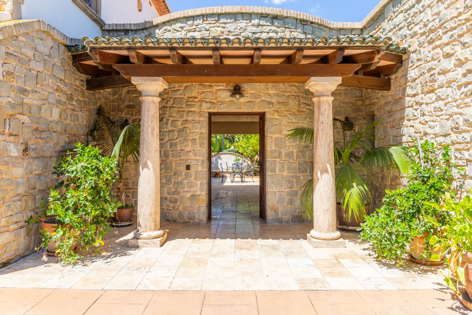 Entrée à portique avec colonnes en pierre et verdure luxuriante.