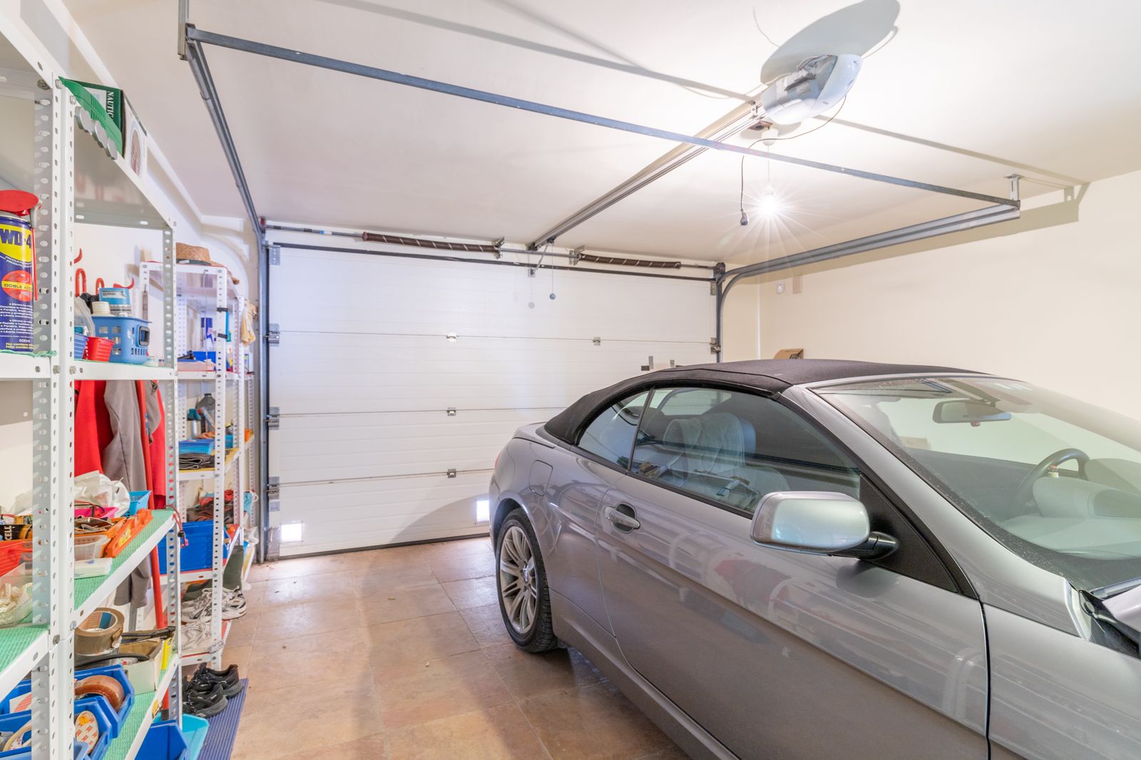 Garage avec étagères métalliques et voiture décapotable grise.