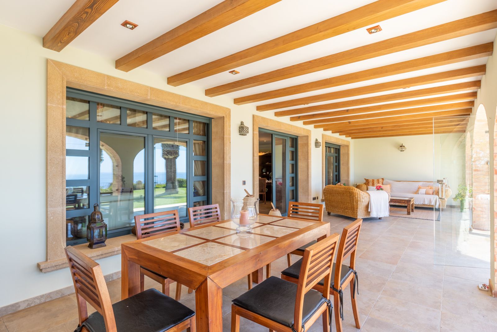 Salle à manger extérieure couverte avec poutres en bois et vue sur le jardin et la mer.